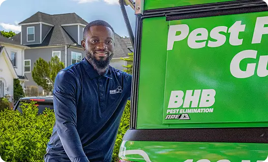 Smiling BHB Pest Elimination technician standing beside a green service van outside a residential home