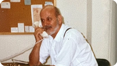 Bald man in white shirt talking on a telephone at a desk in an office