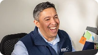 Man in a navy vest laughing while sitting at a desk with a laptop