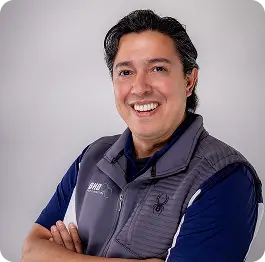 Smiling man with crossed arms wearing a gray vest over a navy polo shirt