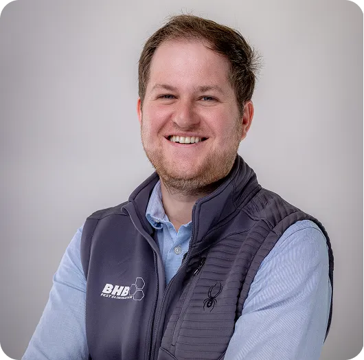 Smiling man in a gray vest over a light blue shirt with a BHB logo, posing for a professional headshot